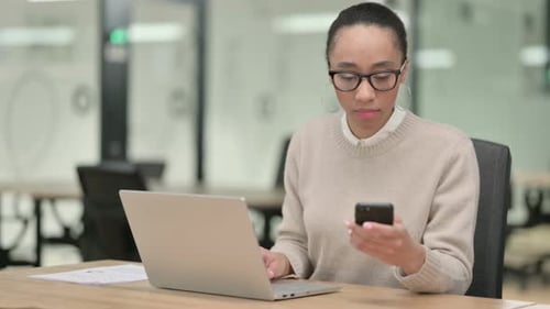 Woman Working on Laptop and Using Smartphone in Office