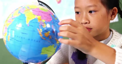 Schoolgirl looking at globe in classroom at school