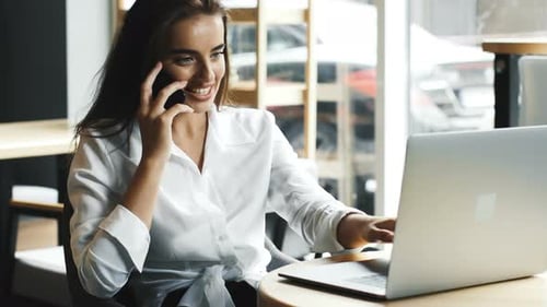 Freelancer Picking Up the Phone Call in the Modern Interior Cafe with Computer at the Table