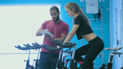 Women Exercising on Stationary Bicycles in Gym