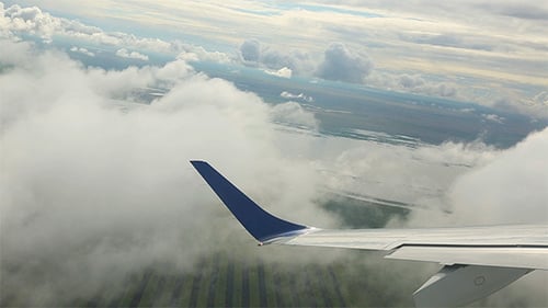 Airplane Wing Flying Above Green Fields and Clouds
