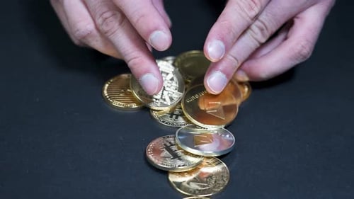 Mains mâles jouant avec diverses pièces de crypto-monnaie en or, surface sombre.