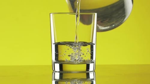 El agua limpia se vierte de la jarra al vaso con muchas burbujas sobre un fondo amarillo en