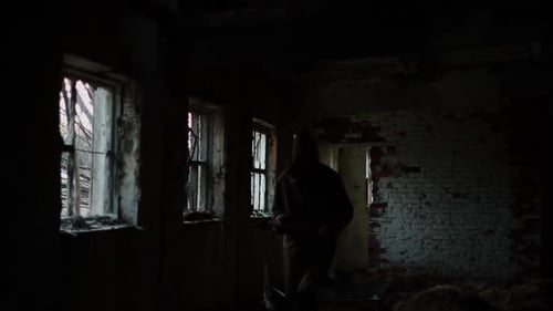 Silhouette of Man in Dark Cloak Walking Through Abandoned Building with an Ax