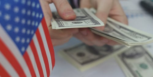 Hands Counting Dollars Next to American Flag