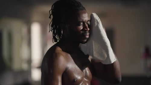 Vue latérale : beau sportif afro-américain épuisé essuyant la sueur avec une serviette expirant