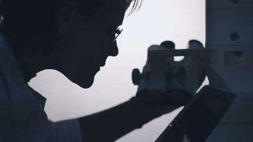 Woman Uses Microscope in Dark Lab Setting