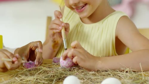 Nettes kleines Mädchen lächelt und bringt Glitzer auf das Osterei