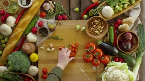 Person Cutting Tomatoes on Wooden Table Surrounded by Food