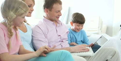 Family Using Laptop Together on White Sofa