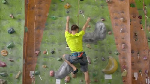 Male Climber Climbs the Cliff Wall in the Room Reaching and Gripping Hold