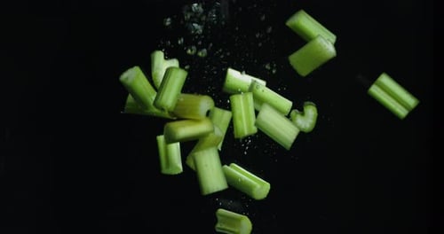 Chopped Celery Falling in Water on Black Background