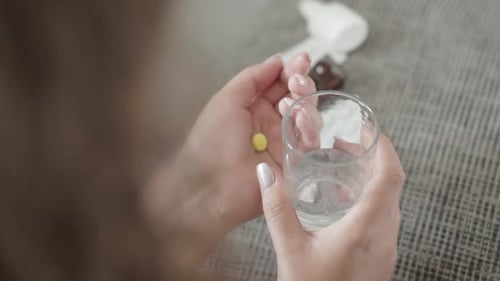 Top Angle View of Female Young Hands Holding Yellow Pill and Glass of Water. Unrecognizable Plus
