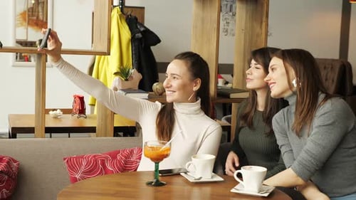 Three Girlfriends are Making Selfie on Mobile Phone Sitting in Cafe
