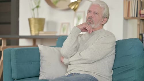 Senior Man Thinking and Sitting on Couch Indoors