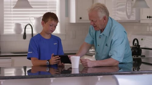 Boy and Senior Man Looking at Tablet in Kitchen