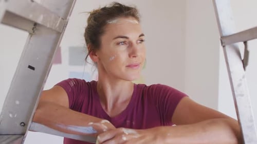 Woman Smiling Covered in Paint Resting on Ladder