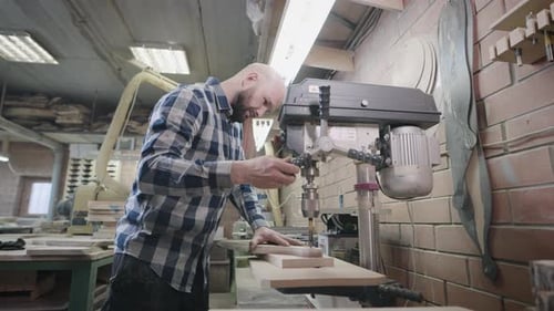 An Experienced Carpenter Works with a Drilling Machine in His Workshop
