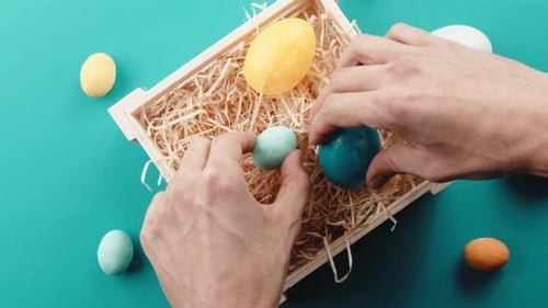 Hands Arranging Colorful Easter Eggs in Crate