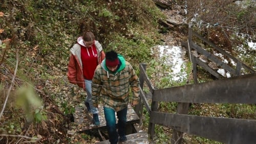 Figures Descending Wooden Stairs Near Mountain Waterfall