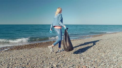 una voluntaria recoge basura en una bolsa de basura negra.