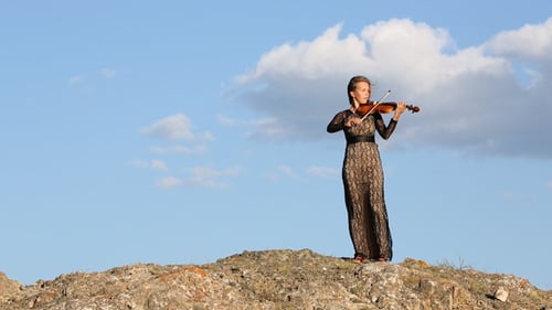 Young Woman Plays Violin Outdoors on Rocky Hill