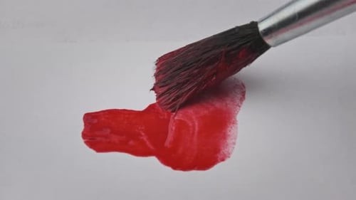 Pinsel mit roter Farbe zeichnet im Makro eine Linie auf weißem Papier