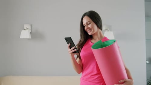 Woman with Yoga Mat Checks Phone Indoors