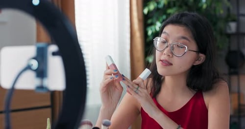 Bloguera de belleza femenina filmando tutorial de rutina diaria de maquillaje usando luz anular con teléfono en trípode