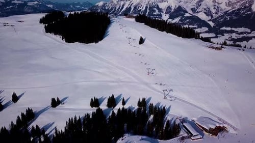 Ski resort in sunny weather. Snow on the ski slope of a wooded mountain. Many tourists near the ski