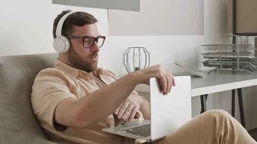 Man Using Laptop and Headphones in Chair