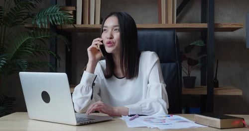 Woman Working with Laptop and Talking on Phone