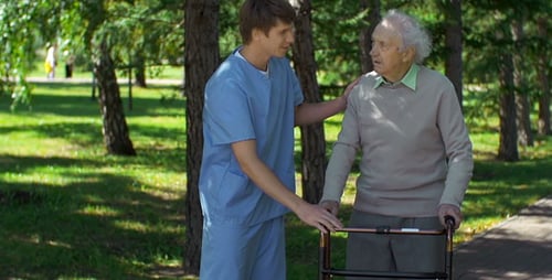 Caregiver Helping Senior Man Walk With Walker