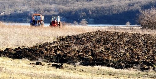 Two Tractors Tilling a Brown Field