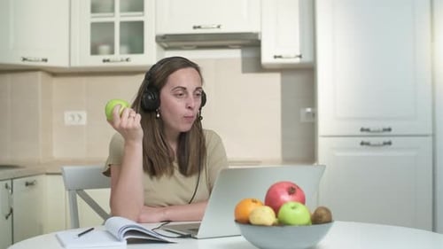 Young Woman Using Laptop and Eating Apple