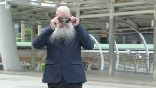 Mature Bearded Bald Businessman Wearing Sunglasses in the City Outdoors
