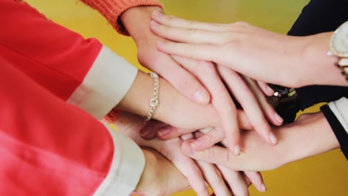Hands Piling in Teamwork on Yellow Background