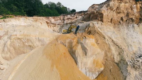 Excavator Working in a Sand Quarry and Extracting Sand. An Excavator Picks Up Sand with a Bucket and