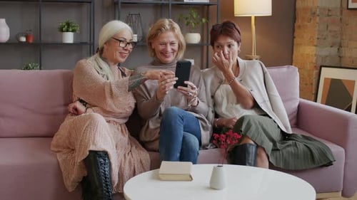 Drei reife Freundinnen schauen sich Fotos auf dem Smartphone an und reden
