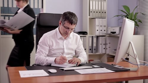 Man Reviews Documents and Writes in Office