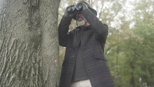 Man Looks Through Binoculars Beside Tree