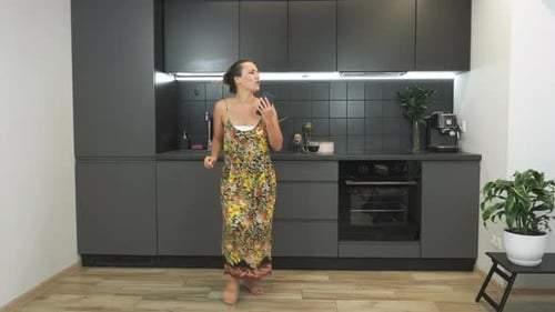 Woman Dances Joyfully in Modern Kitchen with Smartphone