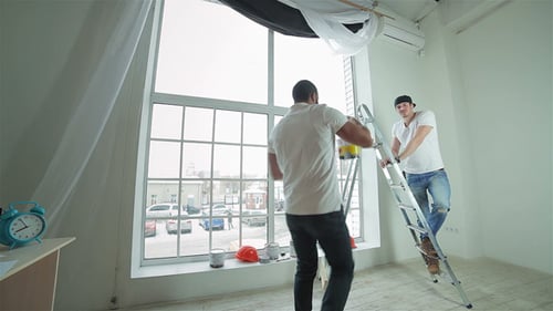 Two Men Painting Indoors Next to Large Window