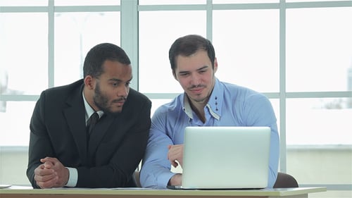 Two Young Men Collaborate on Laptop in Workplace