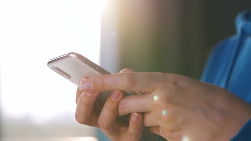 Female Hands Using Smartphone Against the Setting Sun.
