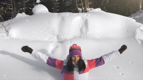 Woman Making Snow Angel in Winter Forest