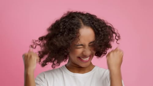African American Female Shaking Fists Gesturing Yes Over Pink Background