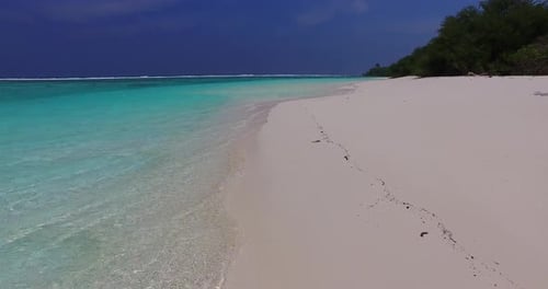 Beautiful flying travel shot of a paradise sunny white sand beach and aqua blue ocean background in