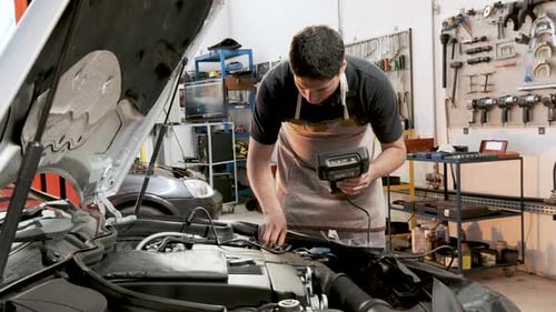 Hispanischer Automechaniker überprüft Auto mit computergesteuertem Diagnoseleser