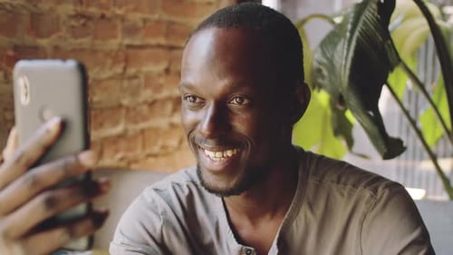 Lächelnder afroamerikanischer Mann Videoanrufe auf Smartphone im Café